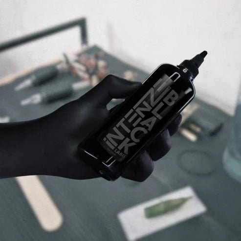 Hand holding a intenze black label tattoo ink with 'Intense Black Label' branding on a blurred background