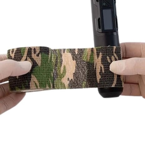 Camouflage tattoo grip tape being applied to a tattoo machine on a white background