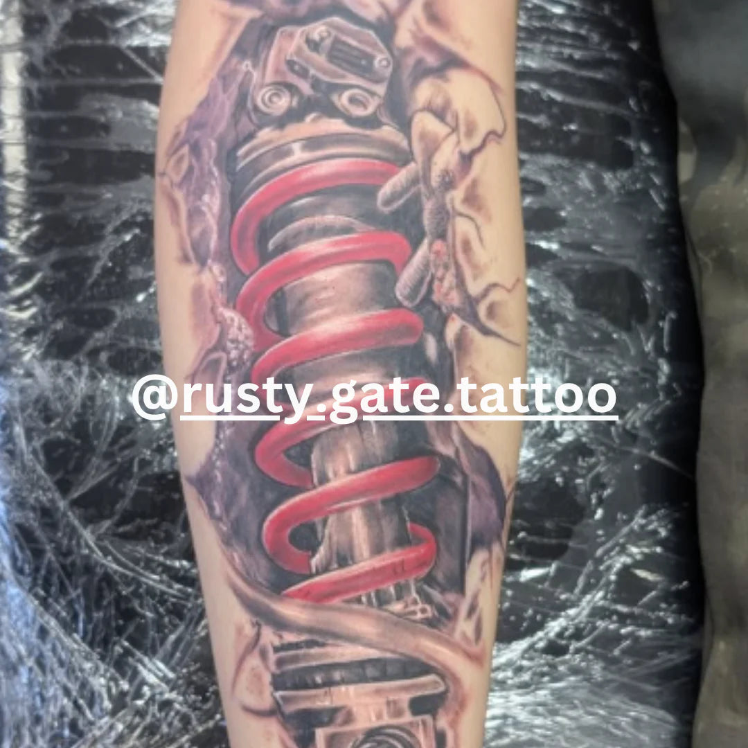 Tattoo of a mechanical spring and gear design on a person's arm, with 'rusty gate tattoo' branding.