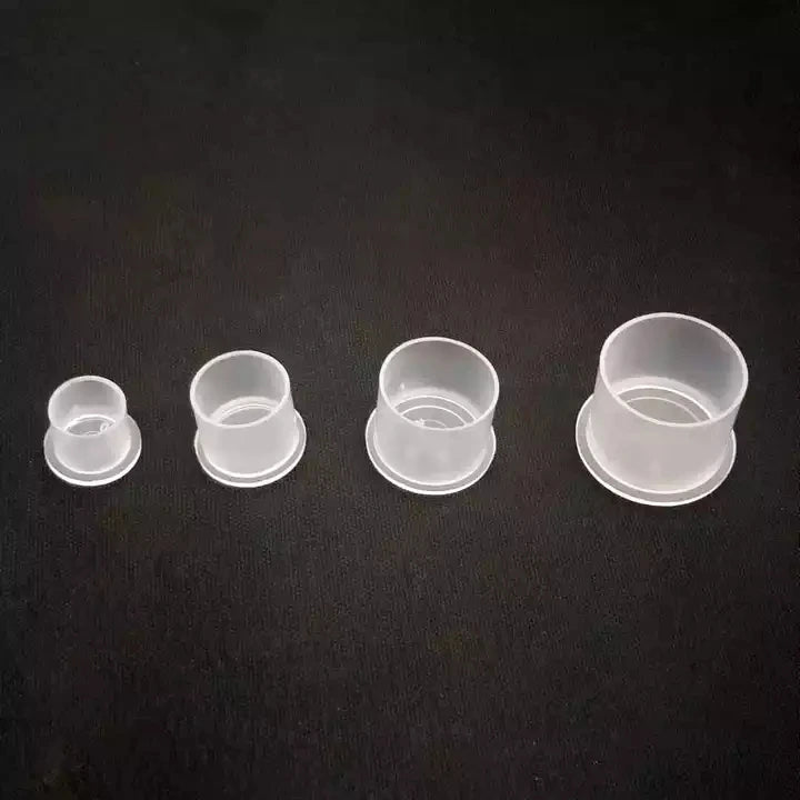 Four clear disposable tattoo ink cups of different sizes on a black background
