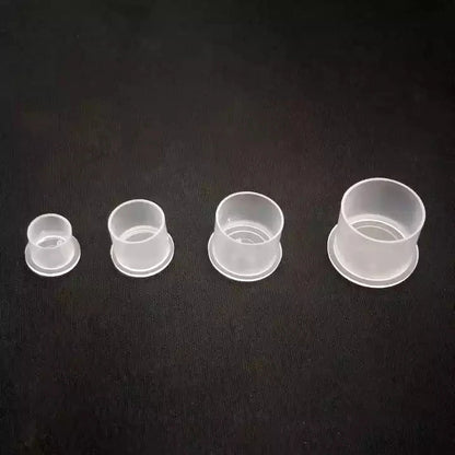 Four clear disposable tattoo ink cups of different sizes on a black background