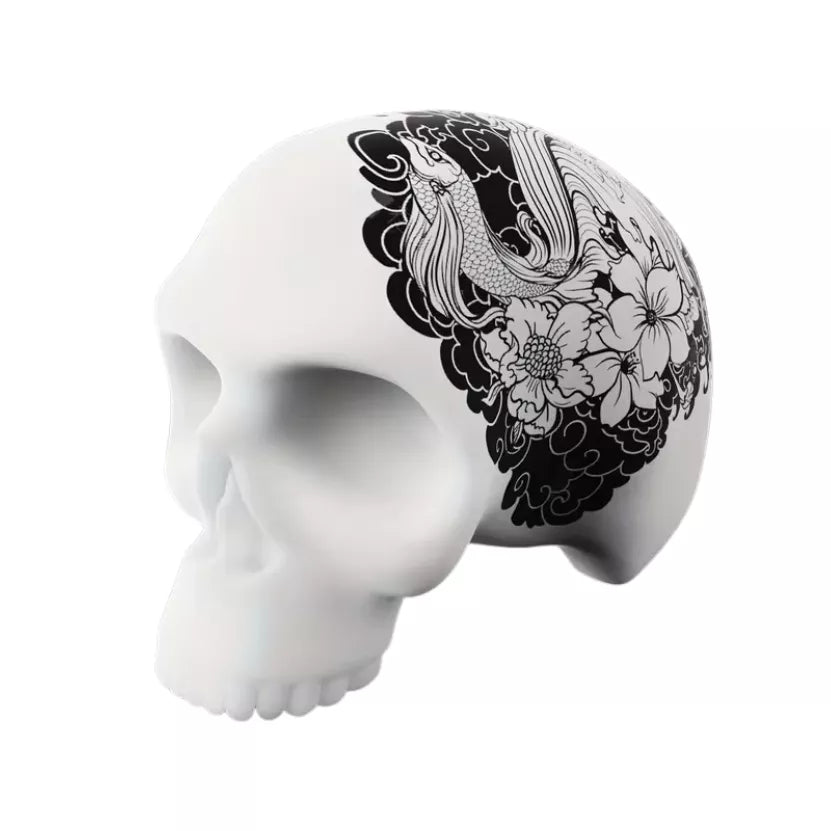 A 3D silicone skull training model for tattoo practice featuring a black and white floral and bird illustration printed on the side, shown against a plain white background.