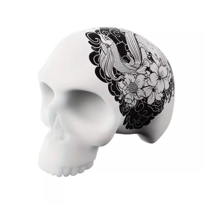 A 3D silicone skull training model for tattoo practice featuring a black and white floral and bird illustration printed on the side, shown against a plain white background.