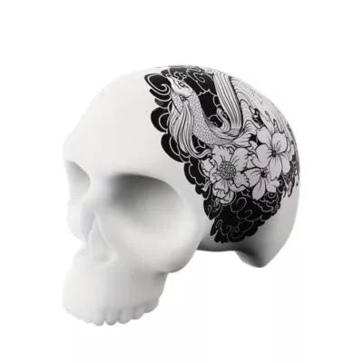 A 3D silicone skull training model for tattoo practice featuring a black and white floral and bird illustration printed on the side, shown against a plain white background.