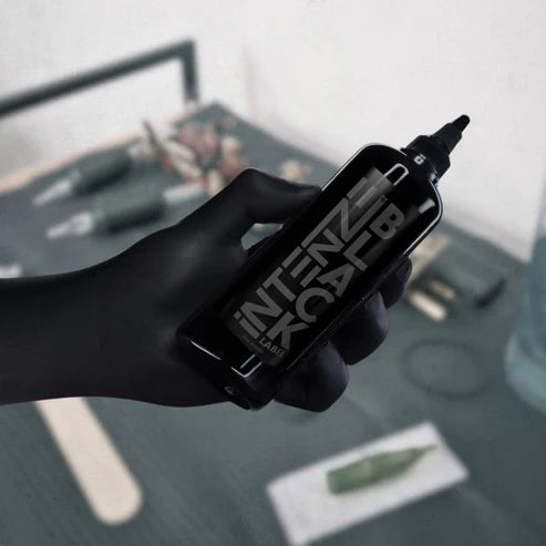 Hand holding a intenze black label tattoo ink with 'Intense Black Label' branding on a blurred background