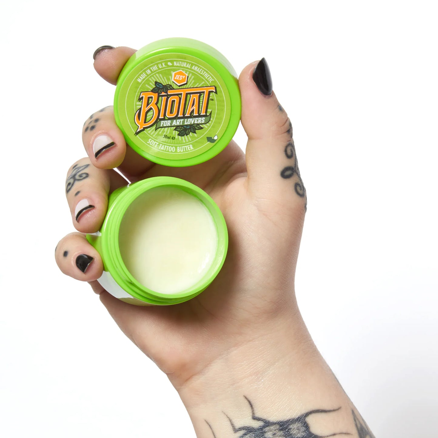 Hand holding an open container of an open 50ml Biotat Zest numbing tattoo butter jar with a white background