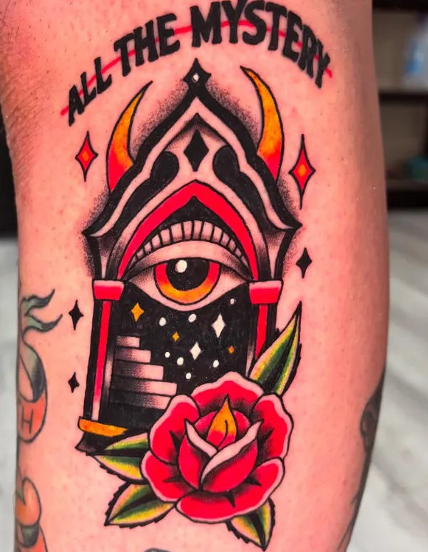 Tattoo of an eye within a temple structure with 'All the Mystery' text, surrounded by a rose.