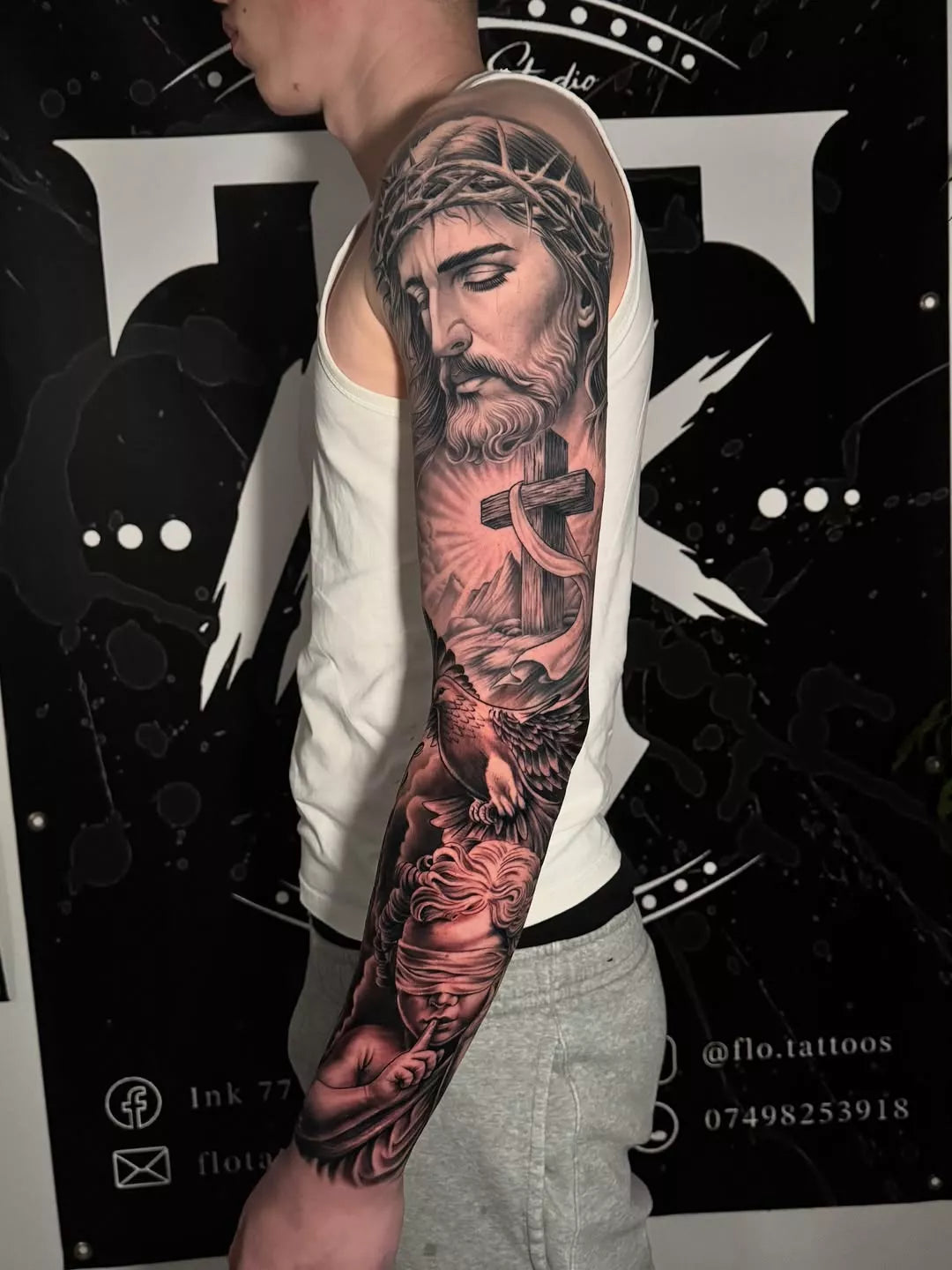 Person with a detailed sleeve tattoo of a religious figure on a black background with branding.