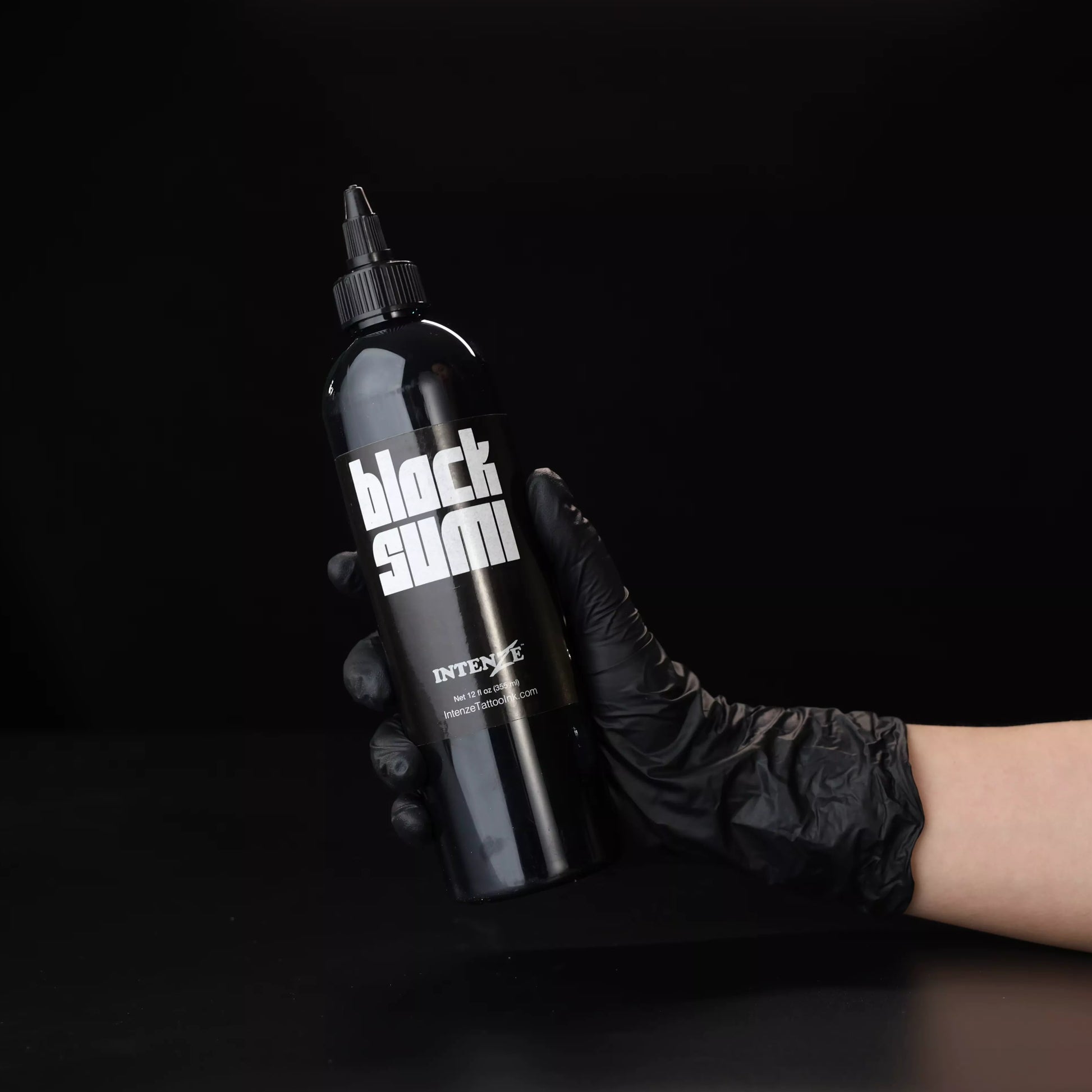 Hand wearing a black glove holding a black bottle of Intenze Japaneze Black Sumi for black and grey tattooing