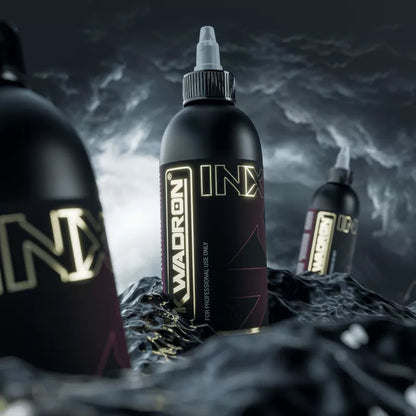 Three Kwadron INX Enriched Black EU REACH tattoo ink bottles, set against a dark stormy sky background with glossy black liquid in the foreground.