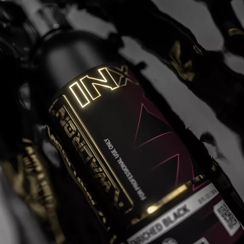A close-up of a Kwadron INX Enriched Black EU REACH bottle, featuring a glossy black and dark red label with gold foil lettering and a white 'Discolored Black' variant label at the bottom.