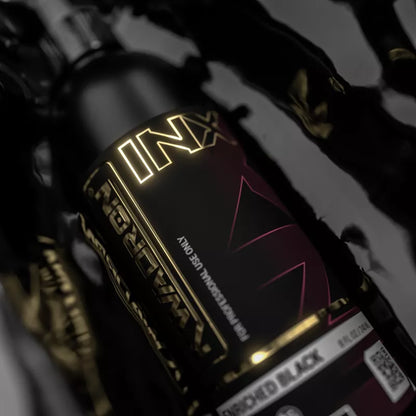 A close-up of a Kwadron INX Enriched Black EU REACH bottle, featuring a glossy black and dark red label with gold foil lettering and a white 'Discolored Black' variant label at the bottom.