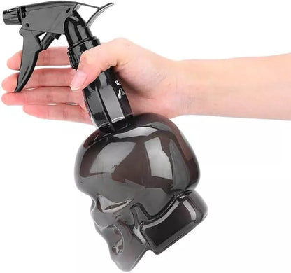 Black spray bottle shaped like a skull held by a hand on a white background